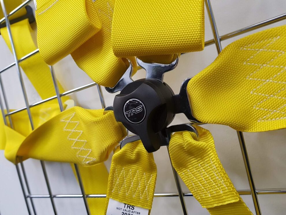 Close up of a yellow TRS six point harness with its black cam lock buckle and the harness label