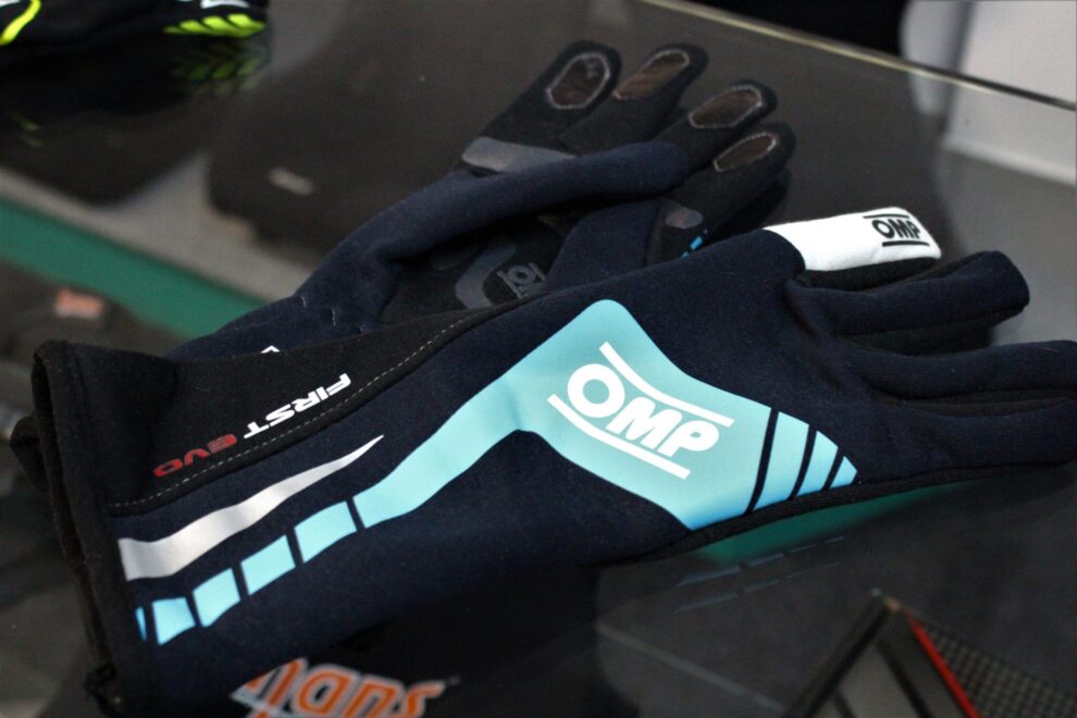 A pair of navy OMP First Evo race gloves with light blue stripes on a glass counter in the GSM Performance showroom