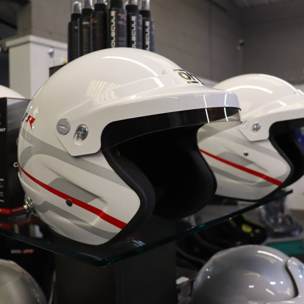 Close up of a white OMP J-R open face helmet with its white peak, tinted visor strip and red and grey side stripes
