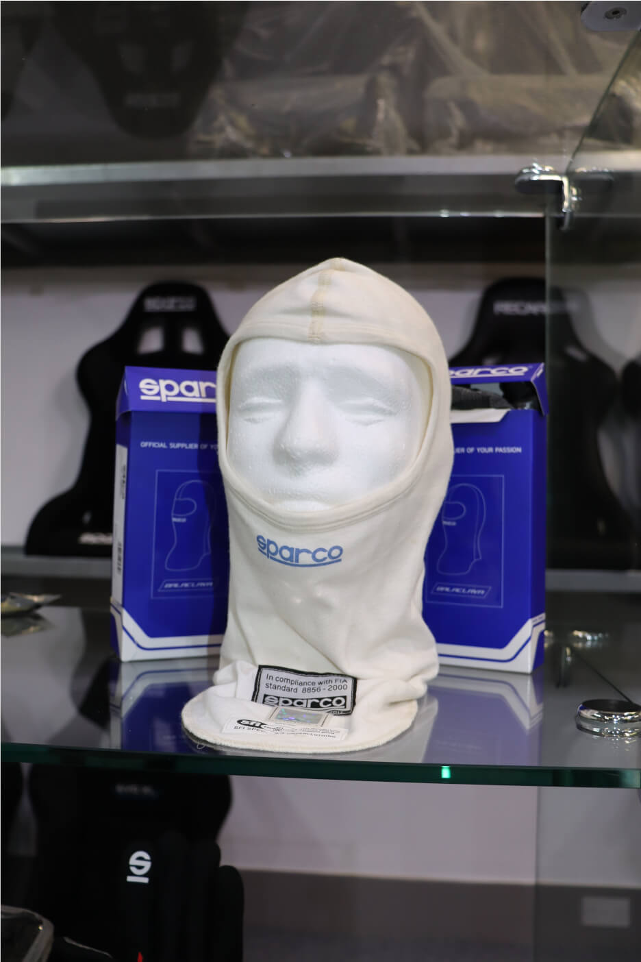 A white Sparco balaclava on a display head between two Sparco boxes on a glass shelf