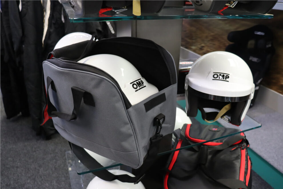 Grey and red Rocked-IT helmet bag holding a white OMP helmet on a glass shelf in the GSM Performance showroom
