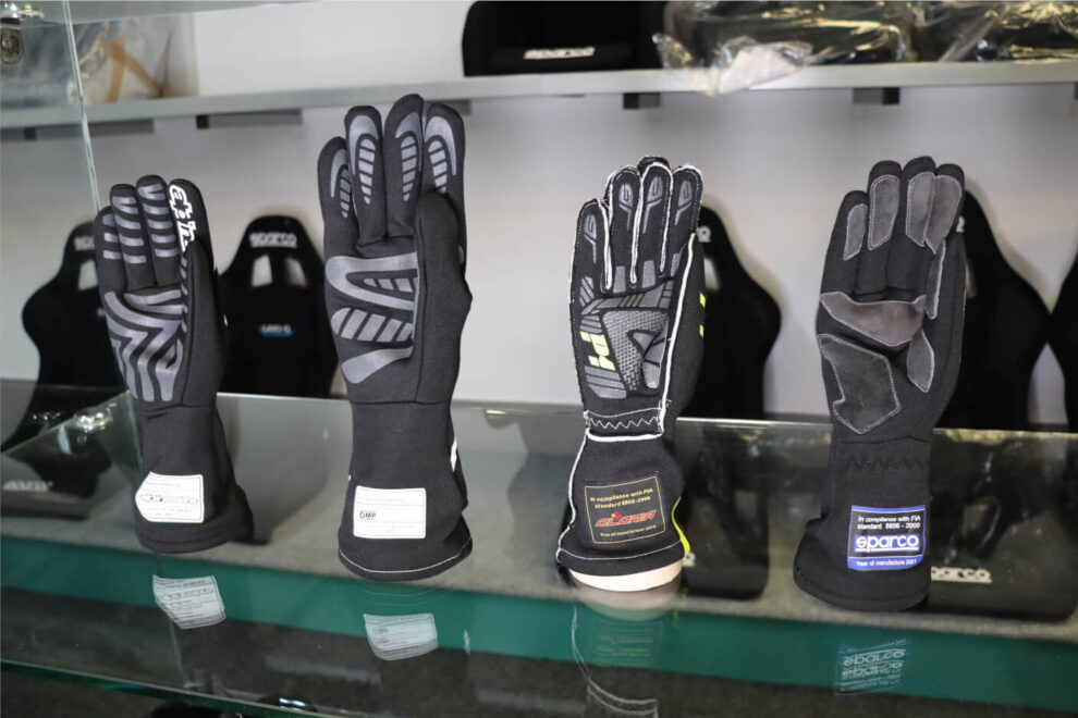 Palms of four race gloves on a glass shelf showing their silicone and suede grip patterns