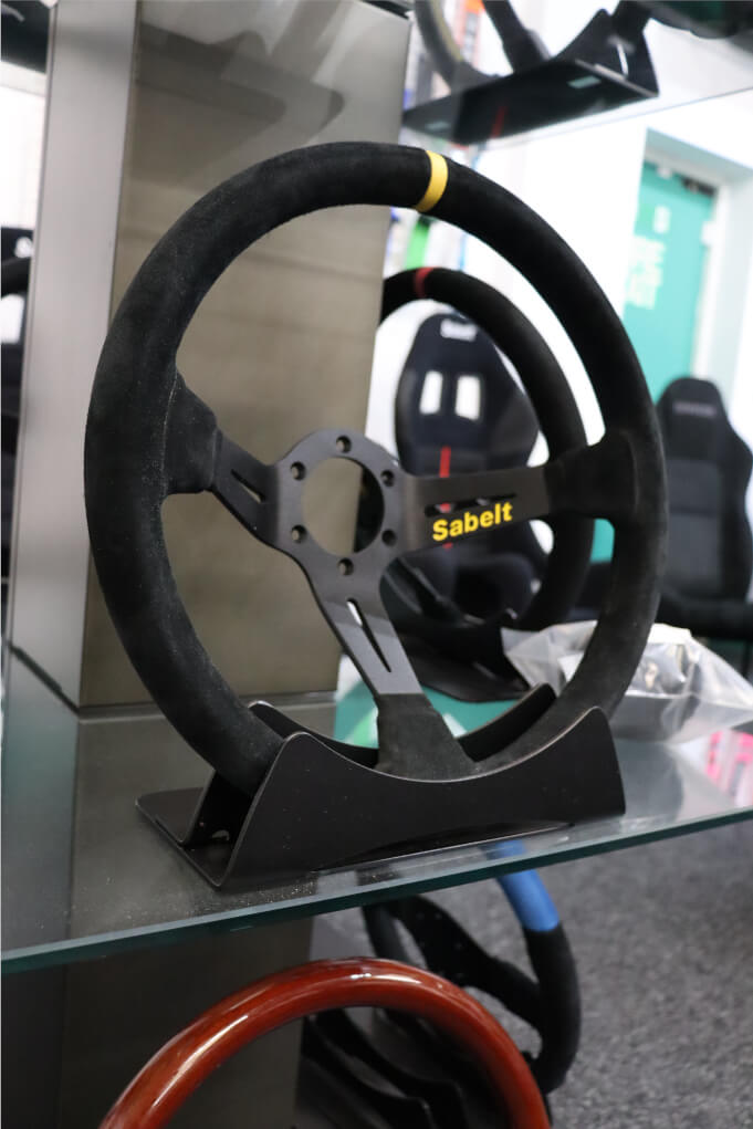 Black suede Sabelt SW-390 deep dish steering wheel with a yellow centre stripe on a display stand