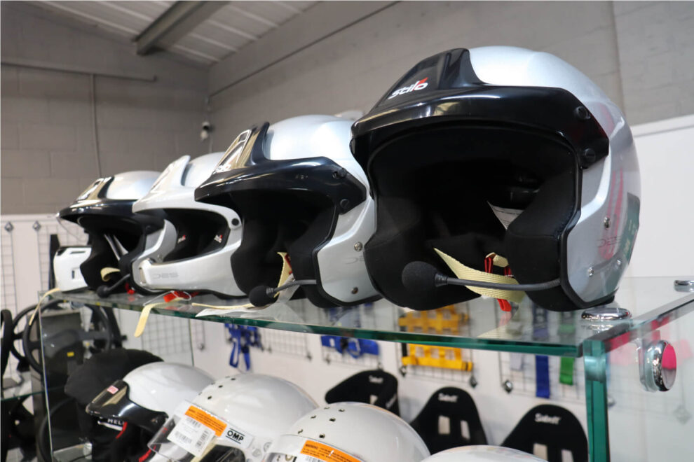 Silver and black Stilo open face helmets with intercom microphone booms on a glass display shelf