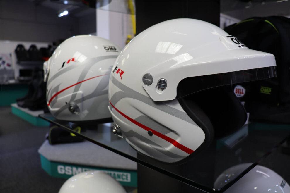 White OMP J-R open face helmet with red and grey graphics and a white peak on a showroom shelf