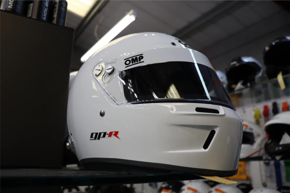 White OMP GP-R full face helmet on a display shelf in the GSM Performance showroom with rows of helmets behind