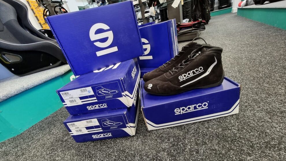 A pair of black Sparco Slalom race boots on top of a stack of blue Sparco boot boxes on the showroom carpet