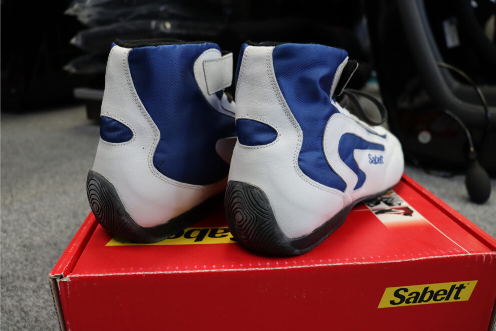 The heels of a pair of white and blue Sabelt RS-400 race boots, showing the Sabelt logo and the dark rubber soles