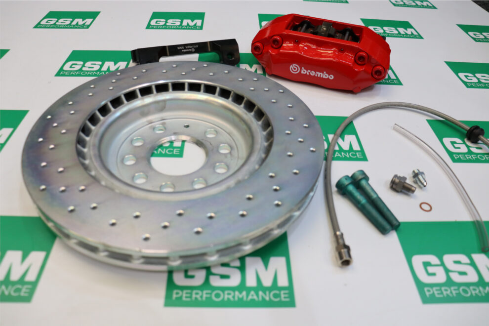 A Brembo drilled brake disc, red four-piston caliper, mounting bracket, braided hose and fittings laid out