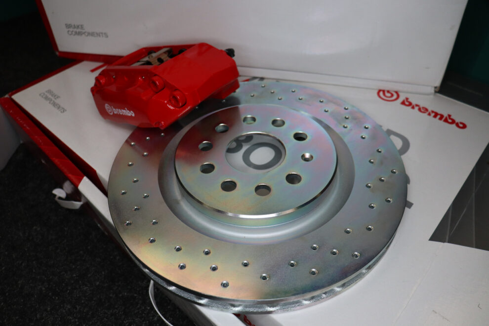 A red Brembo four-piston caliper beside a large cross-drilled brake disc on white Brembo packaging