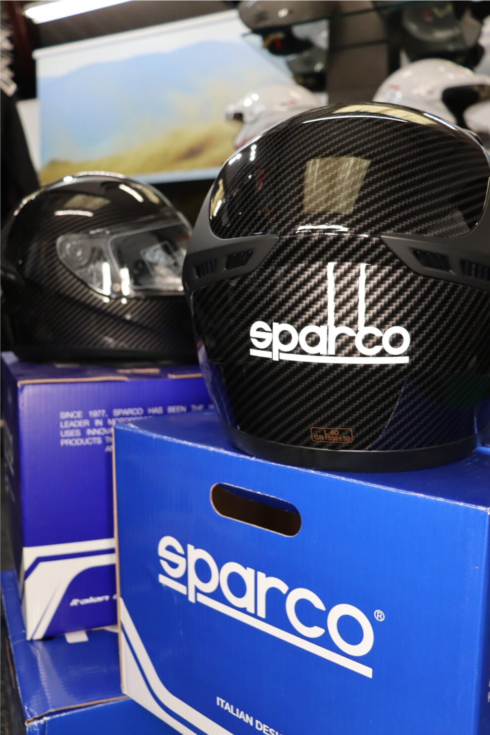 Rear view of a Sparco Club X1 Carbon helmet showing the Sparco logo, sitting on its box