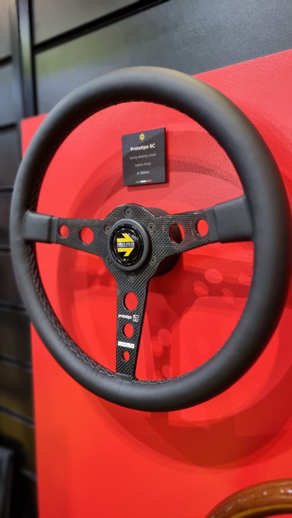 MOMO Prototipo 6C steering wheel with carbon fibre covered spokes on the red wall of the MOMO stand