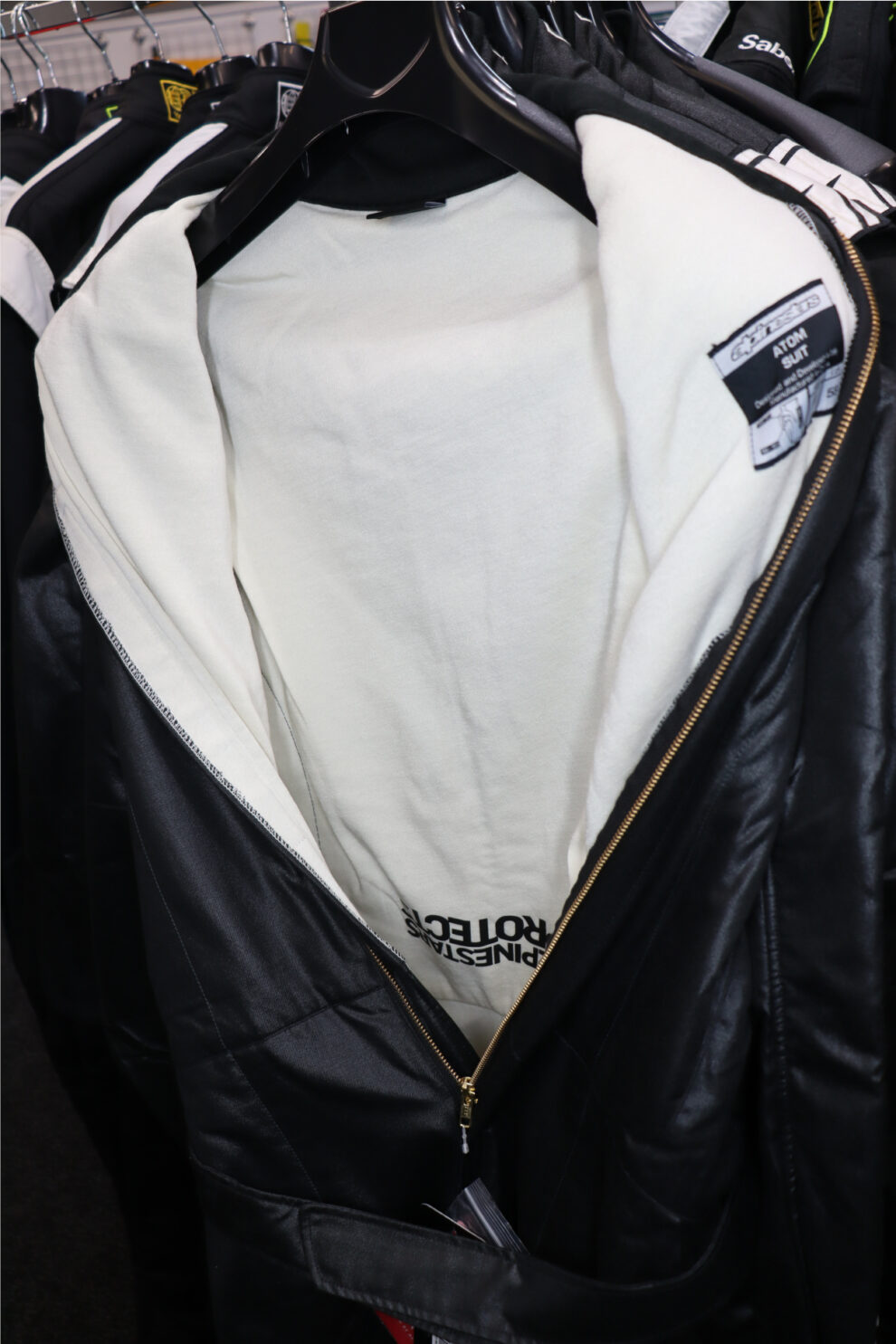 The inside of a black Alpinestars Atom race suit on a hanger, showing the cream Aramidic lining and the Atom suit label