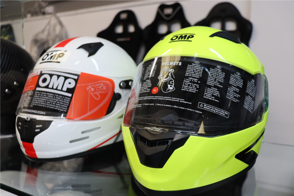 A white OMP helmet and a fluro yellow OMP helmet side by side on a glass shelf in the GSM Performance showroom
