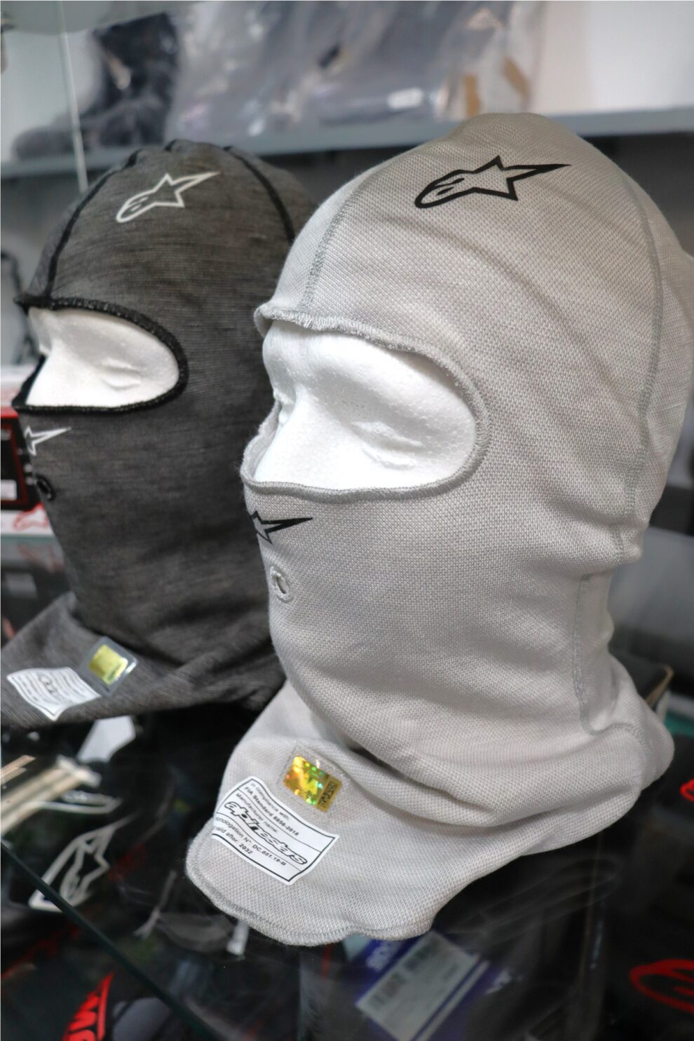 Light grey and anthracite Alpinestars Race V3 balaclavas seen from the side on display heads