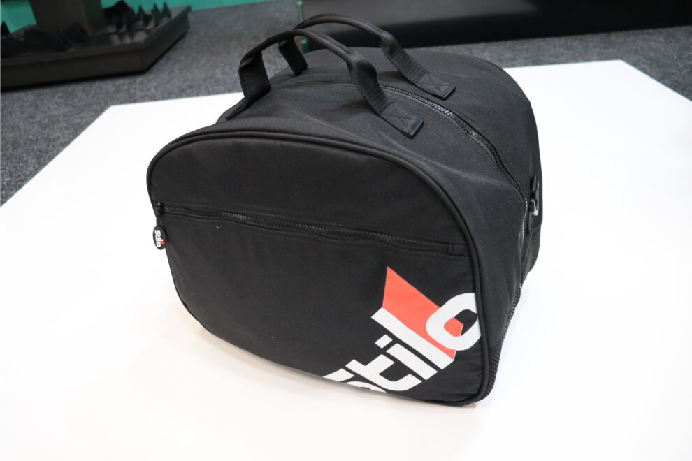 A black Stilo helmet bag with carry handles, a zipped front pocket and a red and white Stilo logo, on a white table in the GSM Performance showroom