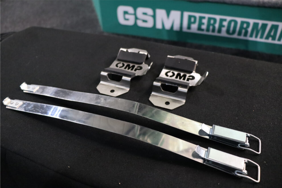 Two OMP stainless steel extinguisher brackets and two quick release steel straps laid out on a black display in the showroom