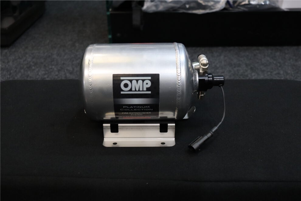 A polished OMP Platinum Collection fire extinguisher bottle with its electrical trigger lead