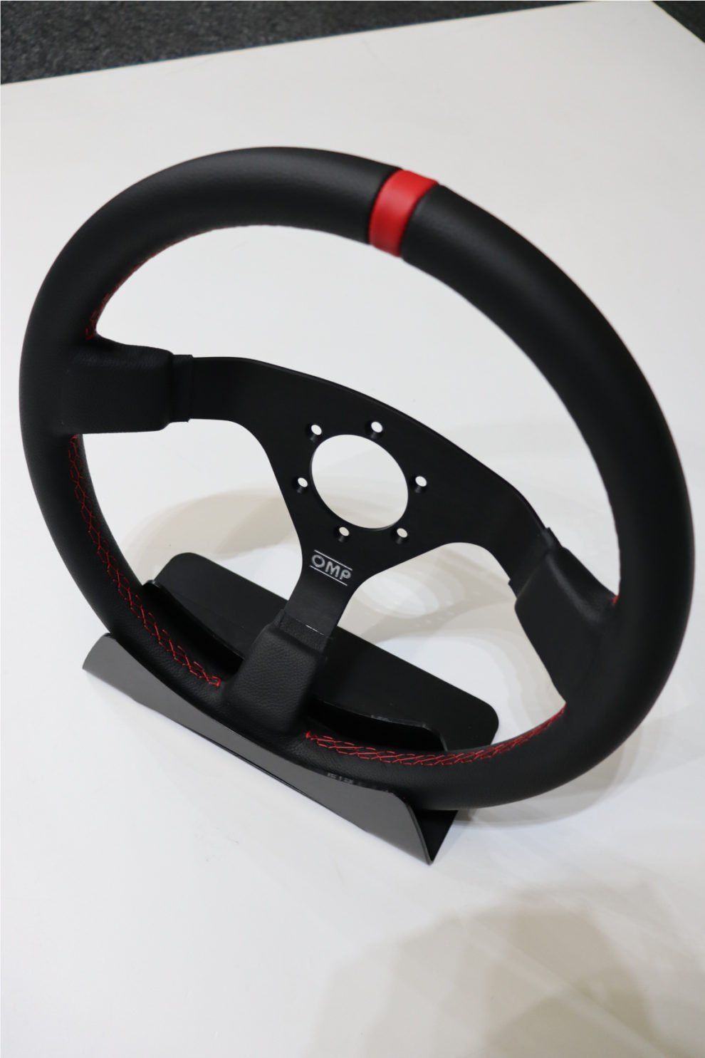 The OMP WRC Red Edition steering wheel in black leather with red stitching and a red top stripe, on a display stand