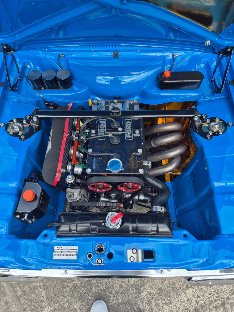 The engine bay of the blue Escort Mk1 showing the Zetec engine, individual throttle bodies with red covers and a polished exhaust manifold