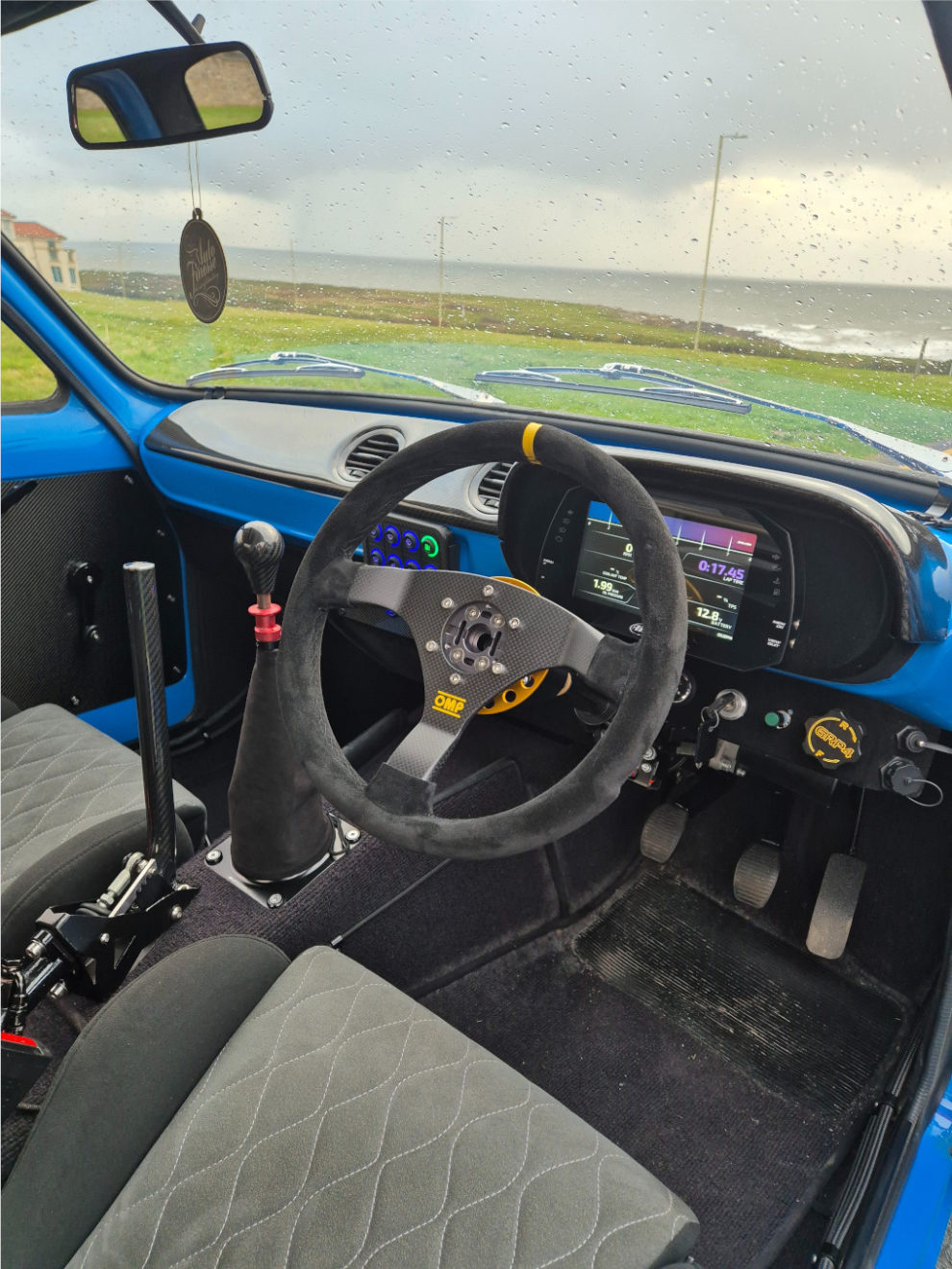 The interior of the blue Escort Mk1 with an OMP Carbon S steering wheel, a digital dash display, quilted seats and a sequential gear lever