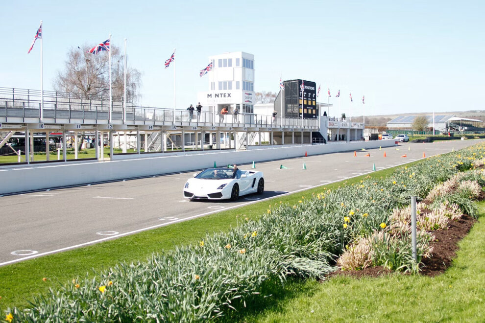 A white Lamborghini Gallardo Spyder on the start straight at Goodwood Motor Circuit, with the pit gantry and flags behind