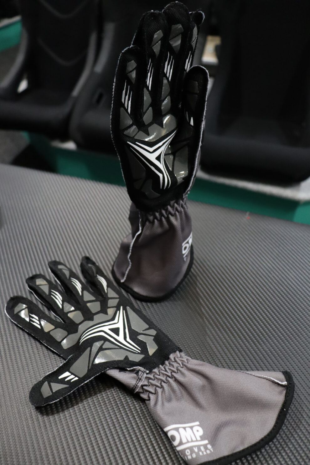 The palms of a pair of OMP KS-2 Art kart gloves showing the grey silicone grip print, on the showroom counter