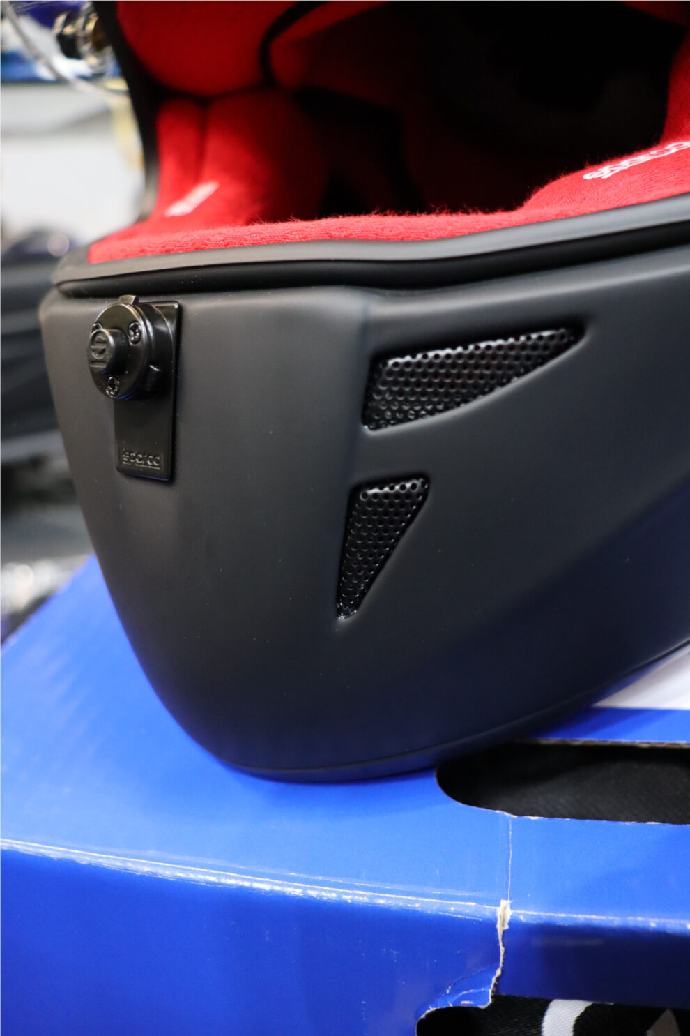 Close-up of the chin bar of a matt black Sparco Stealth RF, showing its two mesh vents and the visor pivot
