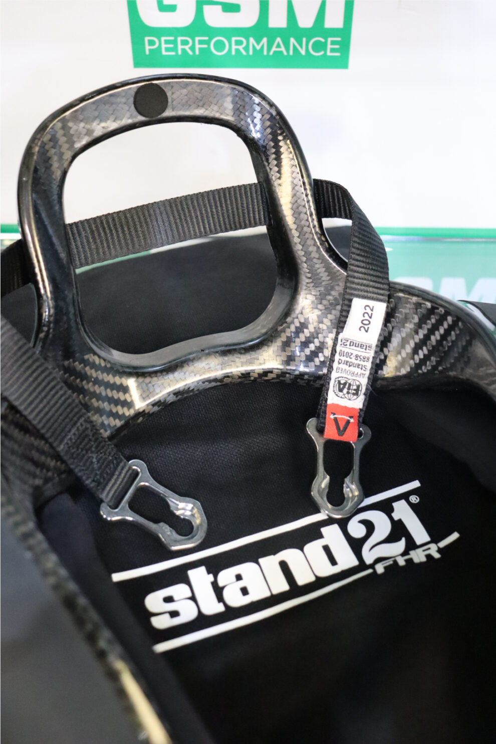 Close-up of the carbon weave on a Stand21 Featherlite HANS device, with its tether label showing FIA 8858-2010 approval