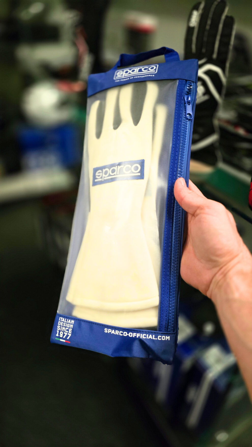 A white Sparco glove in its blue zipped Sparco bag, held up to the camera