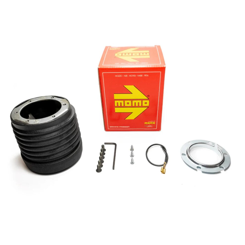 A black MOMO boss kit beside its red MOMO box, with fixing screws, an Allen key, a horn wire and a metal ring laid out