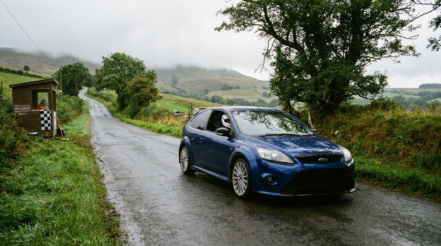 Illustration of a standard road-going hot hatchback waiting at the start line of a British hillclimb with a marshal hut and chequered flag
