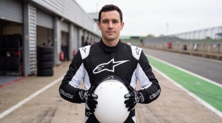 Driver in the Alpinestars Atom race suit in Black and White holding a helmet, wearing Alpinestars Tech 1 Race V4 gloves, in a UK circuit pit lane