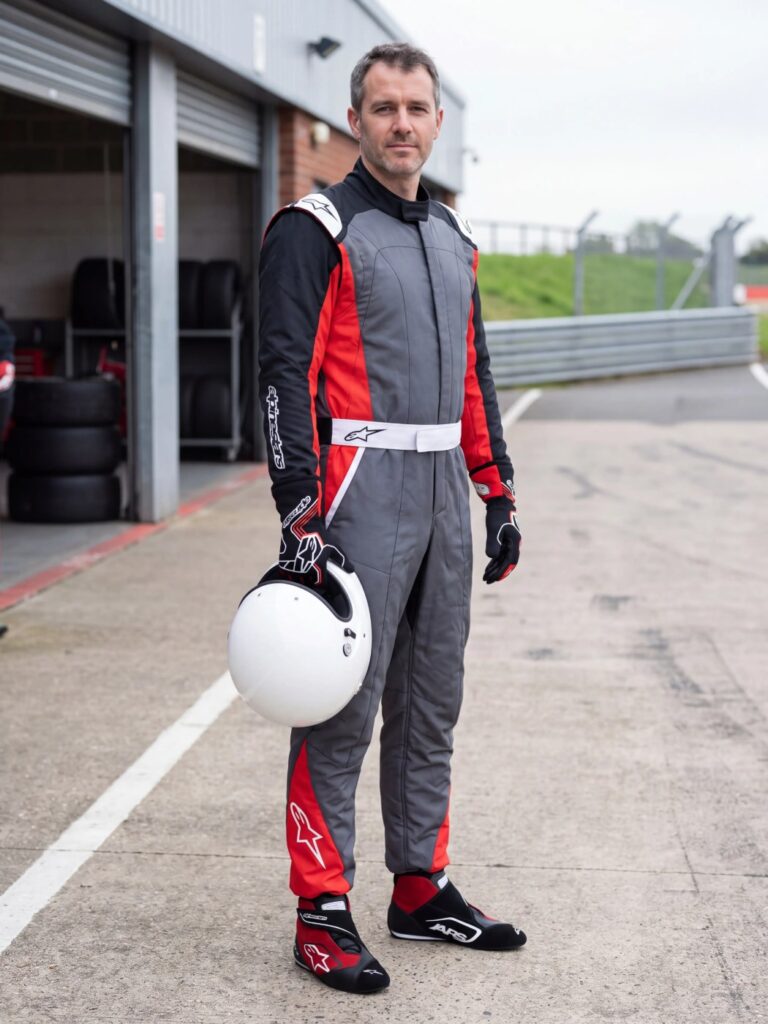 Driver wearing the Alpinestars Atom race suit in Grey, Black and Red with Alpinestars SP+ boots in Black and Red and Tech 1 Race V4 gloves in Black and Red, in a UK circuit pit lane