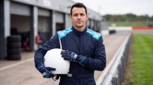 Driver in the OMP First S race suit in Blue holding a helmet, wearing OMP First race gloves in Navy Blue and Light Blue, in a UK circuit pit lane