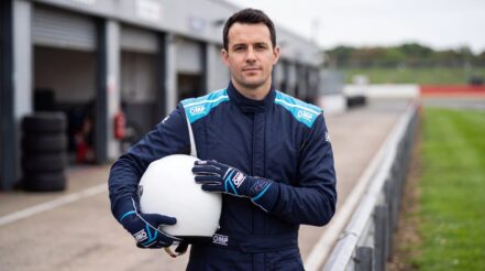 Driver in the OMP First S race suit in Blue holding a helmet, wearing OMP First race gloves in Navy Blue and Light Blue, in a UK circuit pit lane
