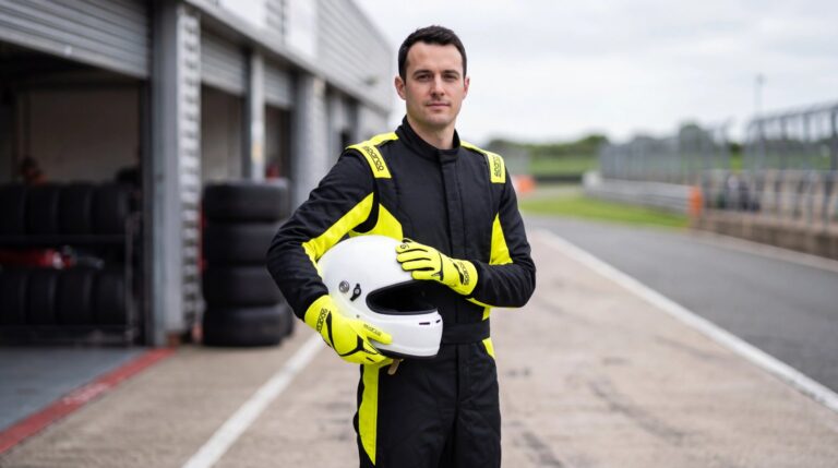 Driver in the Sparco Sprint Advanced race suit in Black and Fluro Yellow holding a helmet, wearing Sparco Land race gloves in Fluorescent Yellow, in a UK circuit pit lane