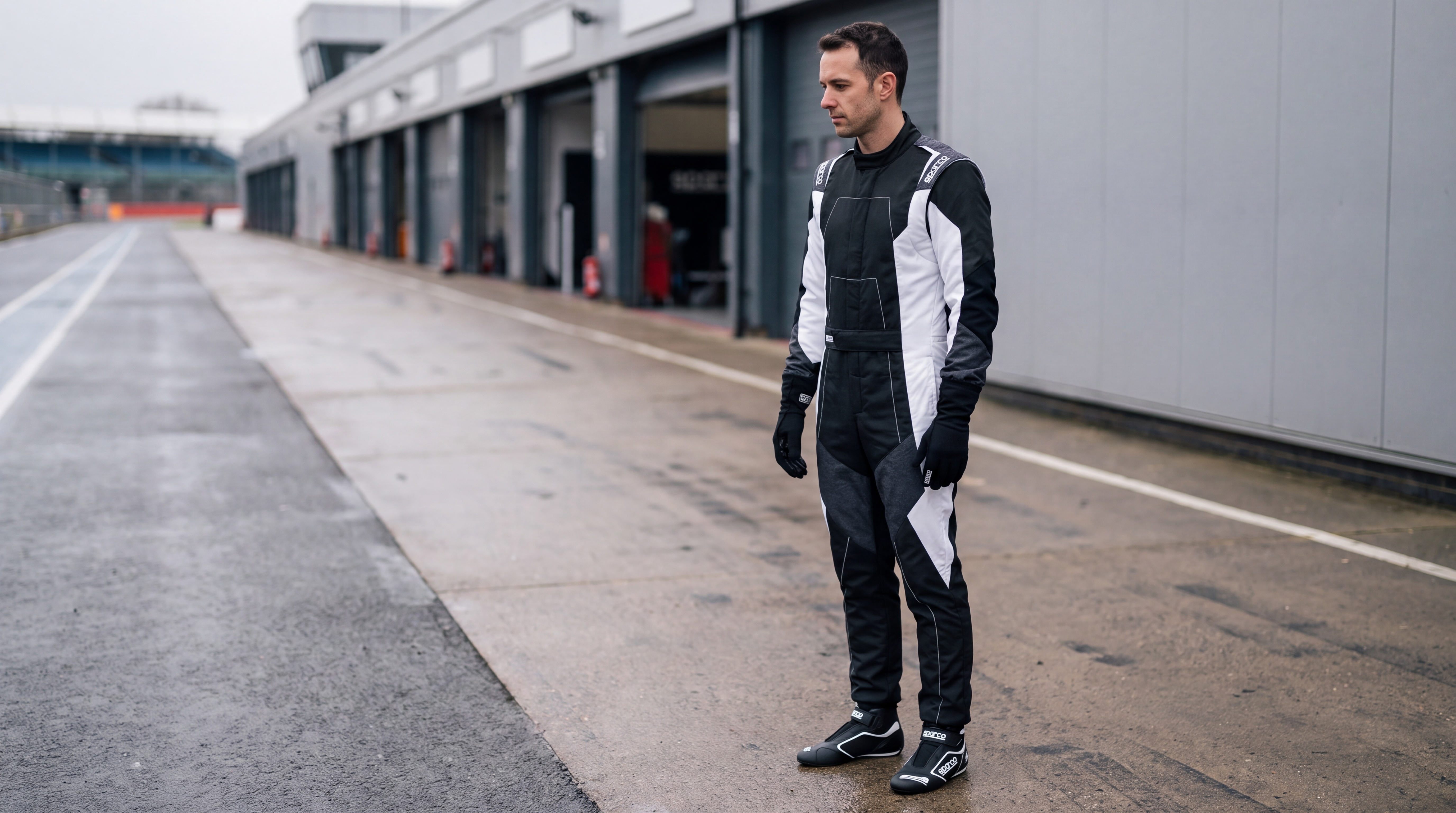 Sparco X-Light set guide — driver in pit lane wearing the black and white X-Light Full Efficiency suit, X-Light Plus boots and Tide+ gloves