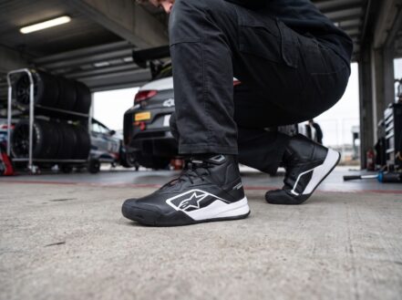 Alpinestars Radar V2 mechanics shoes worn by a mechanic crouched beside a race car wheel in a pit garage