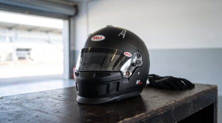 Bell R7 Sport full face racing helmet resting on a workbench in a race circuit garage with racing gloves beside it