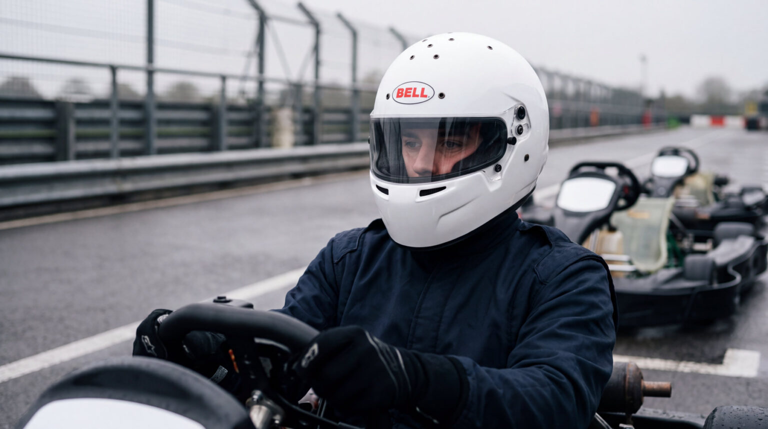 Kart driver sat in his kart in the pit lane wearing a white Bell RS7-K helmet with the visor down