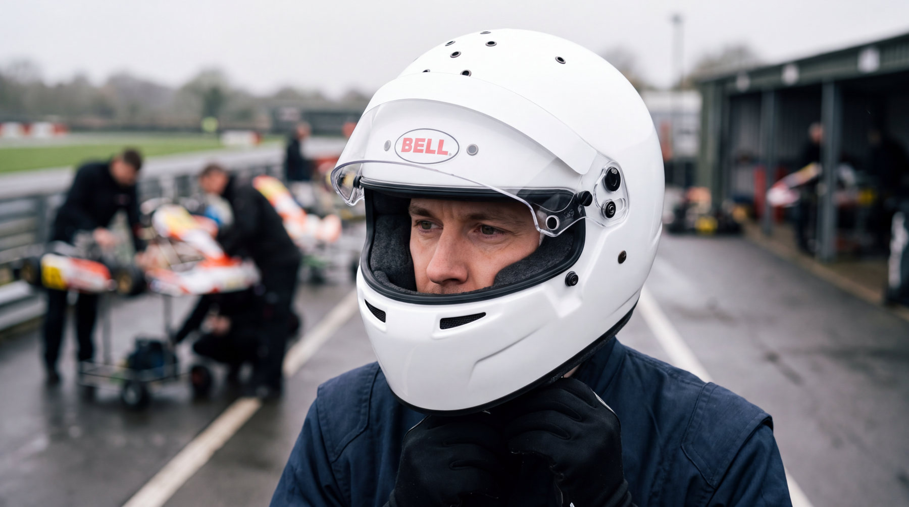 Kart driver in a pit lane wearing a white Bell RS7-K kart helmet with the visor up