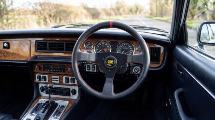 Classic Jaguar XJ6 interior photographed from the driver's seat, fitted with an OMP three-spoke steering wheel. An AI illustration generated from our own product photography.