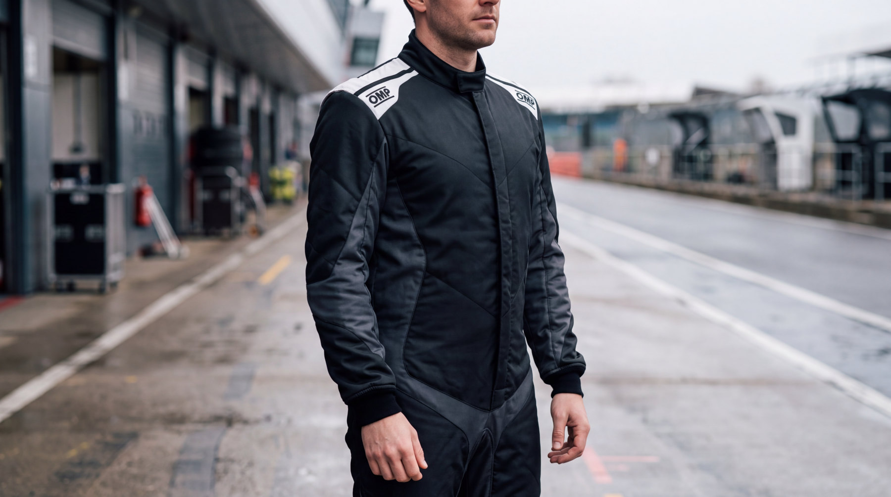 Driver in a pit lane wearing a black OMP One Evo X race suit with white OMP shoulder panels