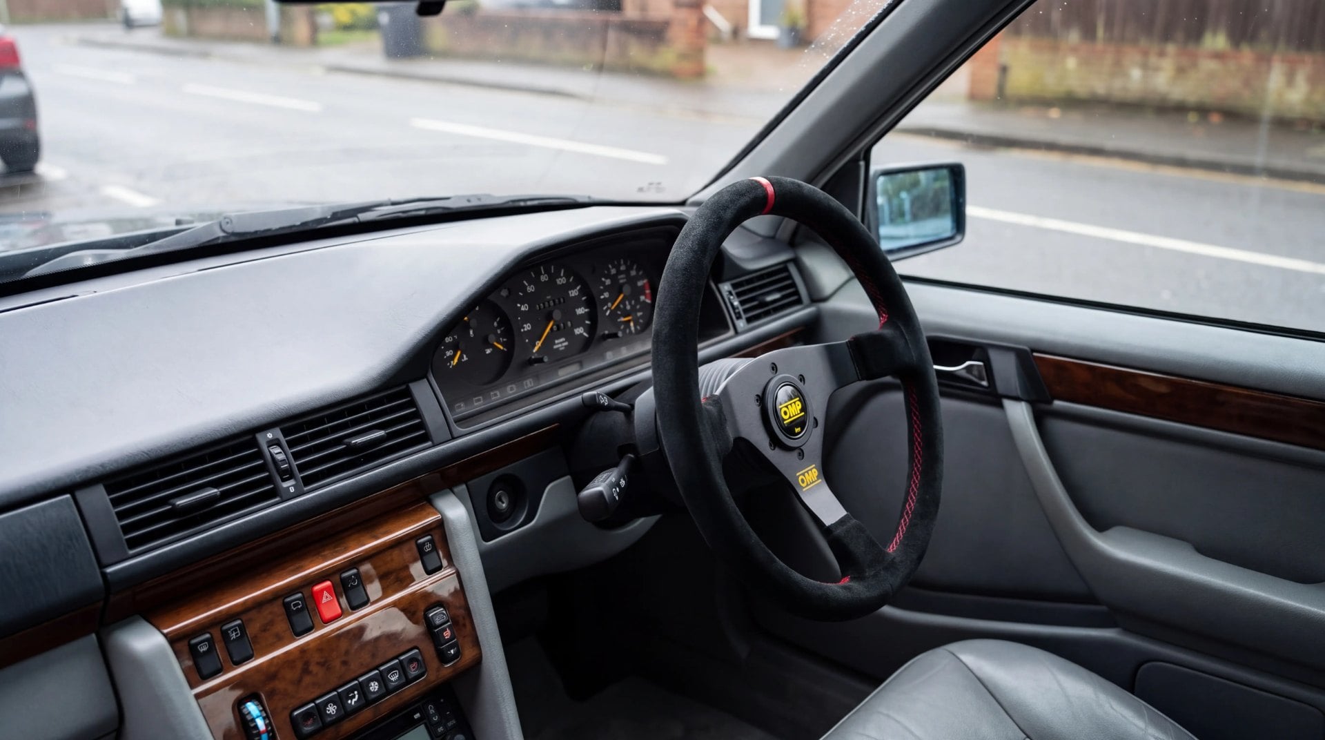 Black suede OMP steering wheel on a boss kit in the right hand drive cabin of a Mercedes W124 E Class