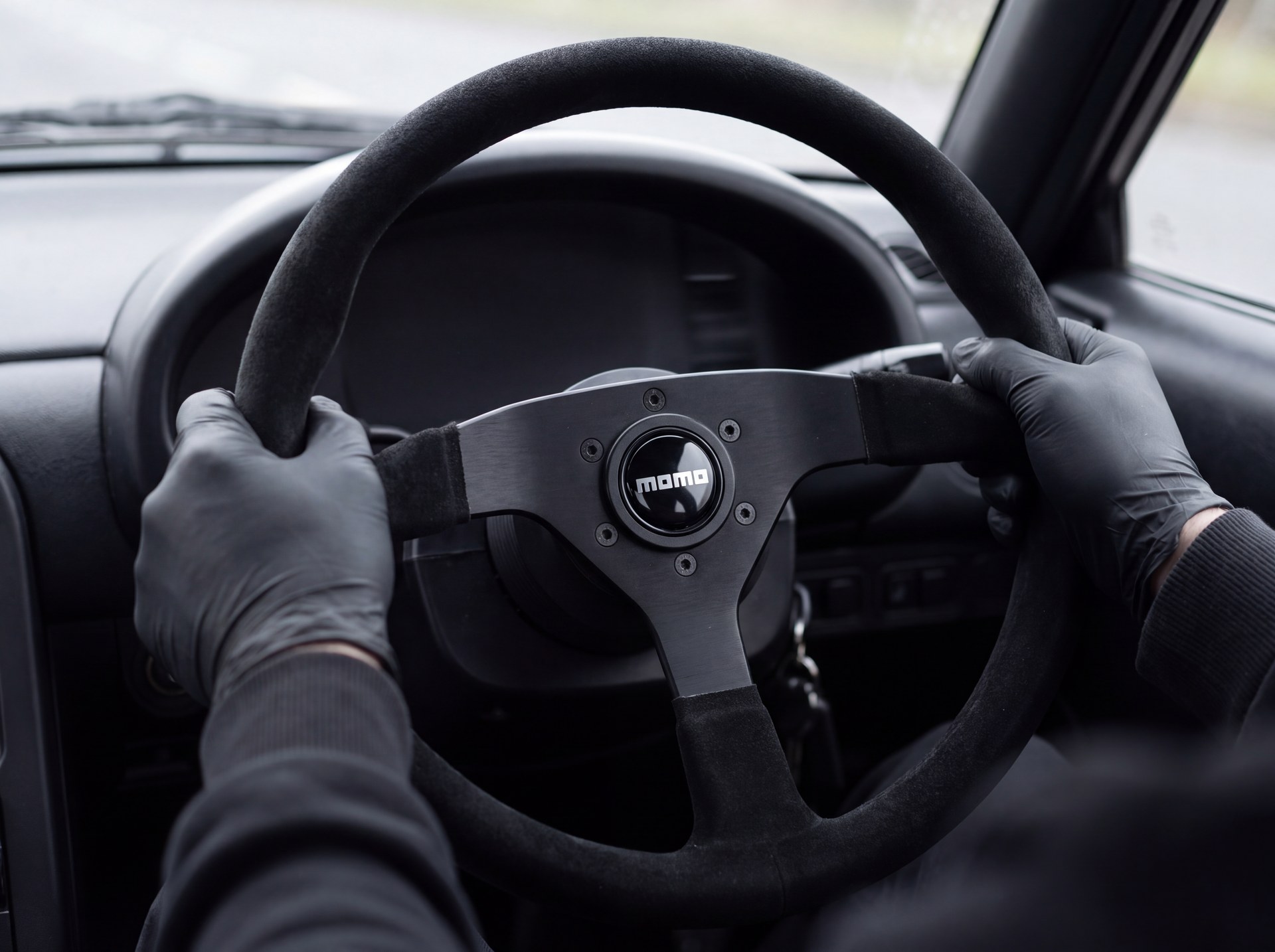 Driver holding a shallow dish black suede MOMO steering wheel on a boss kit in a modified road car