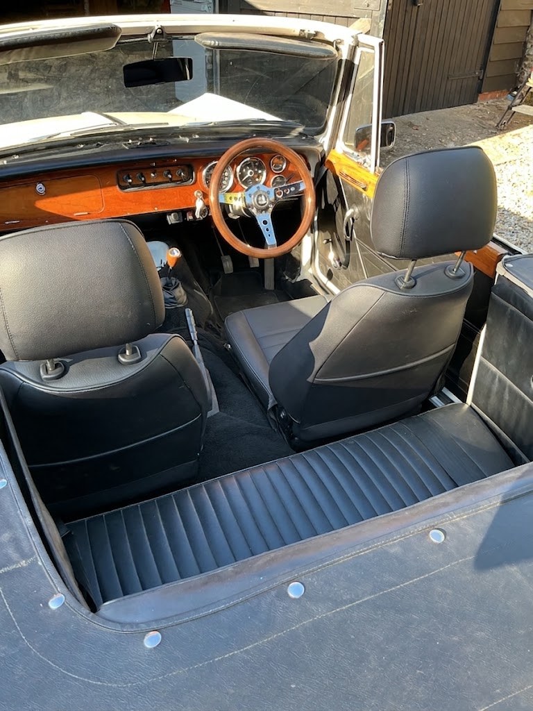 The interior of a Triumph Vitesse convertible looking across the car, showing the wood dashboard, the fitted wood rim wheel and the rear bench seat