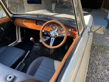 The wood dashboard and OMP Mugello wood rim steering wheel of a Triumph Vitesse convertible, photographed from outside the driver door