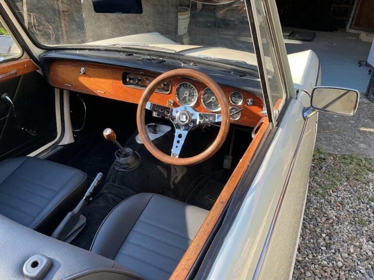 The wood dashboard and OMP Mugello wood rim steering wheel of a Triumph Vitesse convertible, photographed from outside the driver door