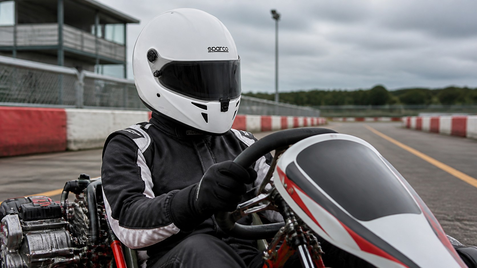 Kart driver seated on circuit wearing a white Sparco Stealth CMR competition kart helmet